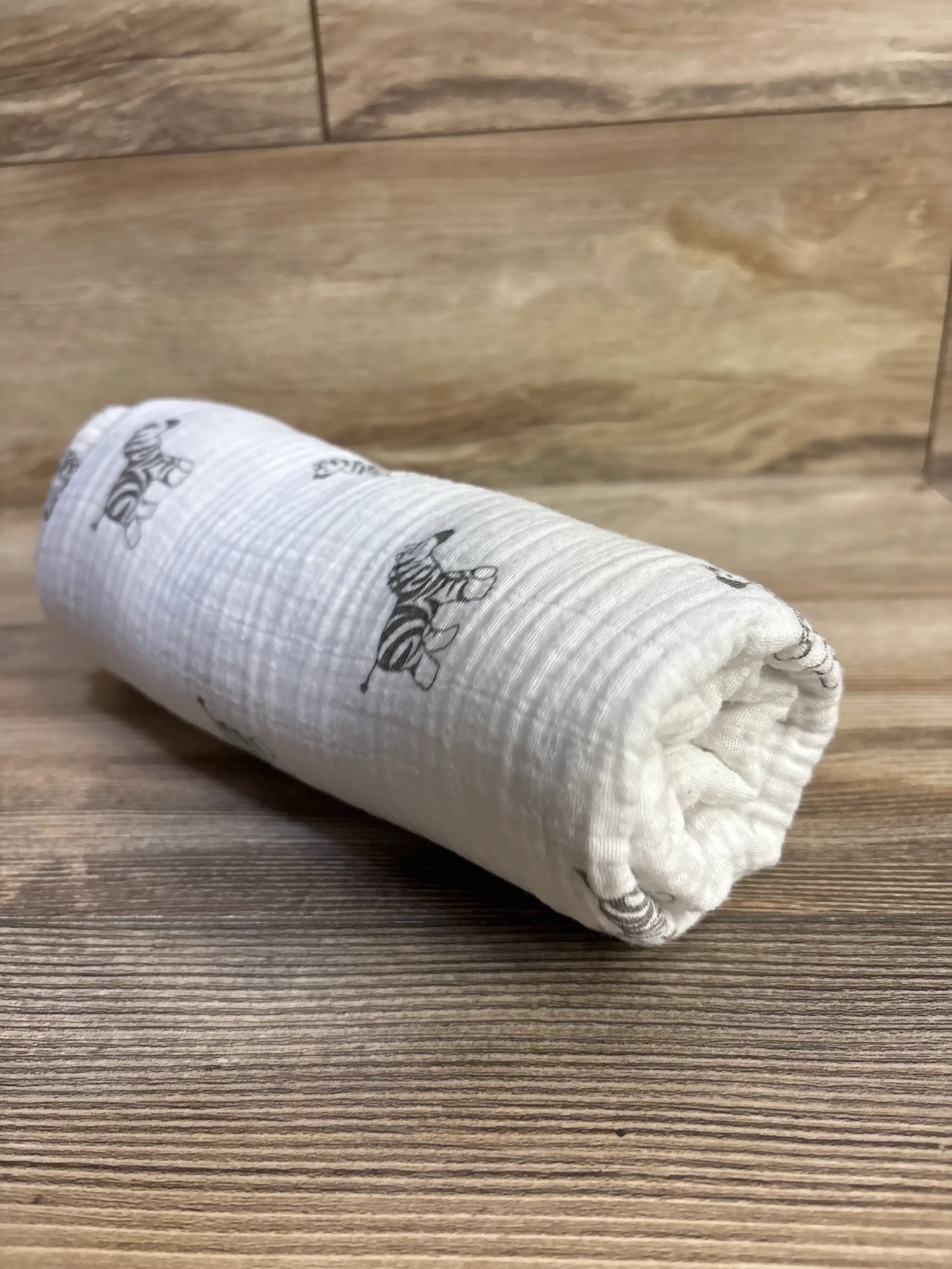 Angled view of Amazing Baby muslin swaddle blanket showcasing zebra print on white muslin fabric with a wood background