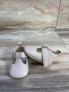 Front and side view of First Steps beige soft sole baby shoes showing scalloped T-strap on wood background