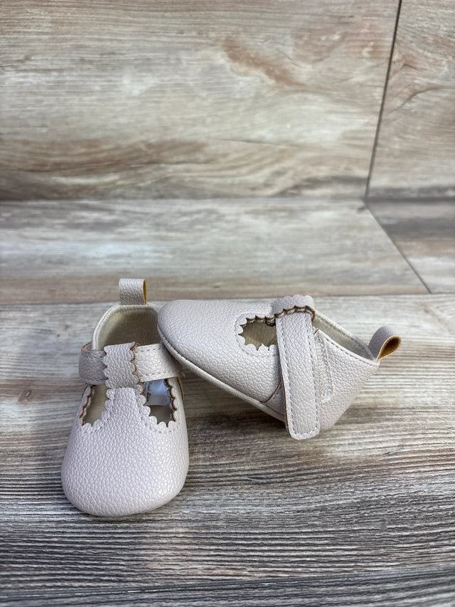 Front and side view of First Steps beige soft sole baby shoes showing scalloped T-strap on wood background
