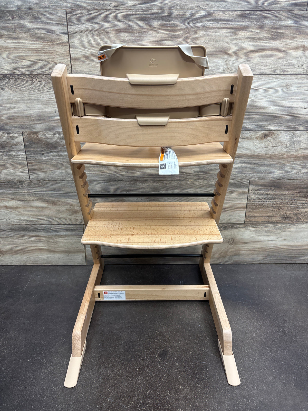 Front view of Stokke Tripp Trapp high chair with tray in Wild Wood Natural showcasing adjustable footrest with wood-panel background