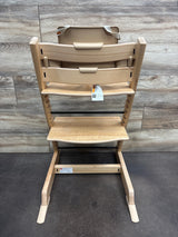 Front view of Stokke Tripp Trapp high chair with tray in Wild Wood Natural showcasing adjustable footrest with wood-panel background