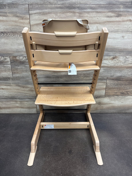 Front view of Stokke Tripp Trapp high chair with tray in Wild Wood Natural showcasing adjustable footrest with wood-panel background