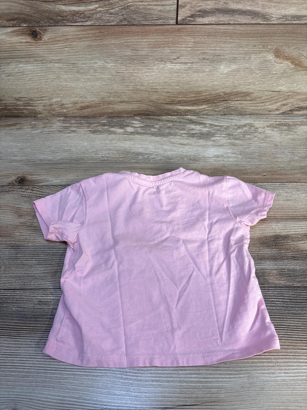 Light pink short sleeve toddler t-shirt on wood background, gently used kids clothing
