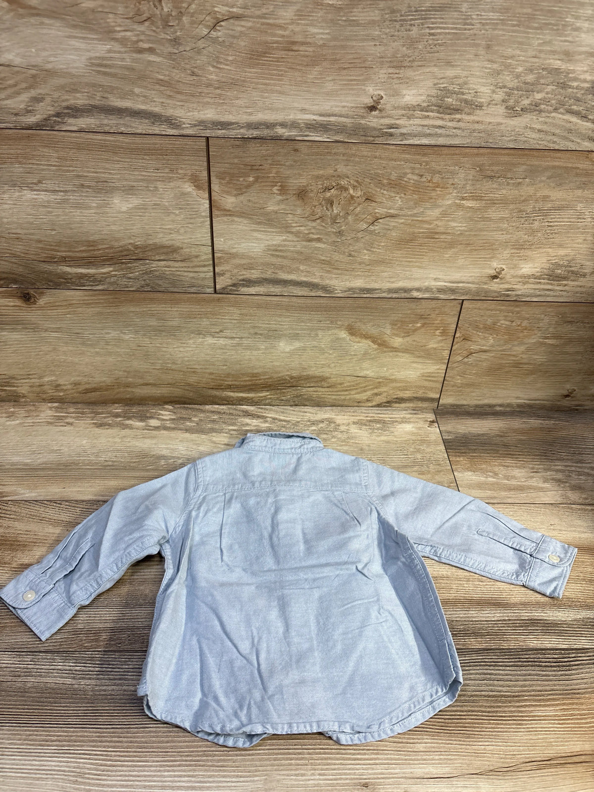 Light blue Baby Gap button-up shirt for infants size 12-18m on a wood background