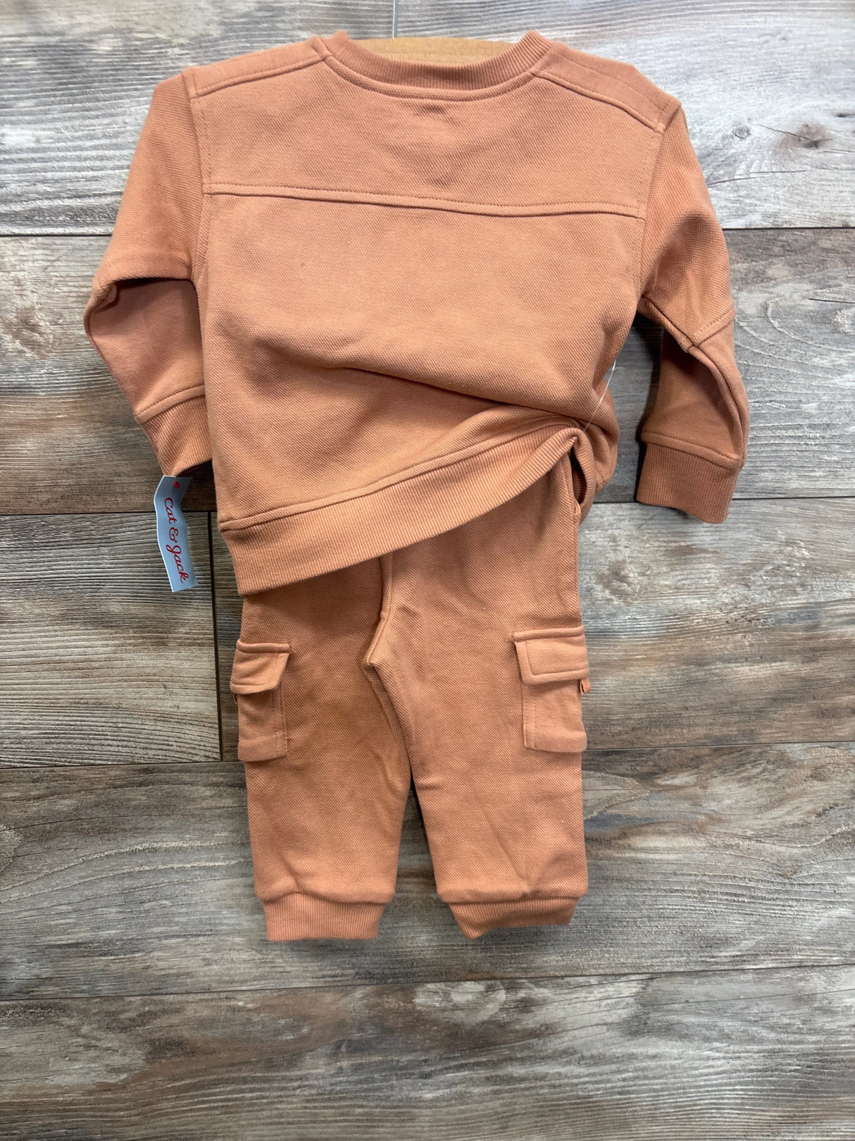 Flat lay of Cat & Jack 2pc pocket crewneck sweatshirt and joggers set in orange showcasing cargo pockets and ribbed cuffs on wood floor