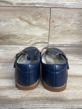 Rear view of Felix and Flora T-strap Mary Jane flats in navy showing stitched heel seam, buckle strap and brown soles on wood floor