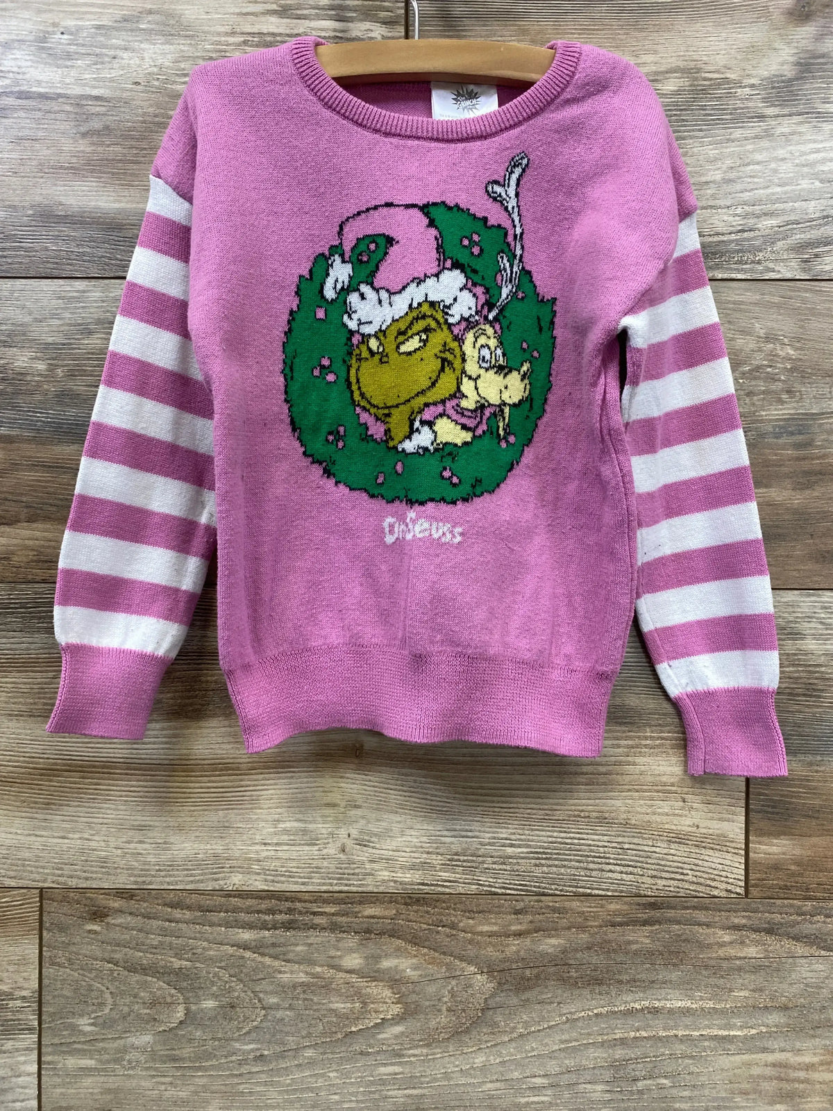 Pink Grinch holiday sweater with striped sleeves, featuring Dr. Seuss characters on a wooden background.