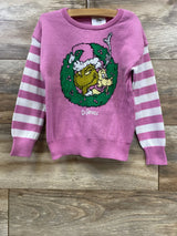 Pink Grinch holiday sweater with striped sleeves, featuring Dr. Seuss characters on a wooden background.