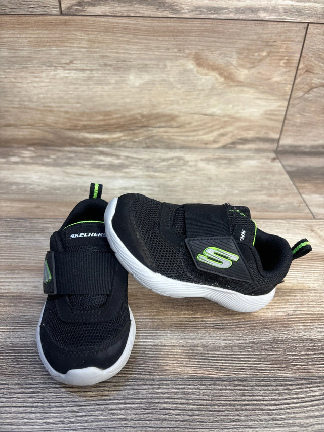 Black Skechers toddler athletic shoes with green accents and Velcro straps on wood floor