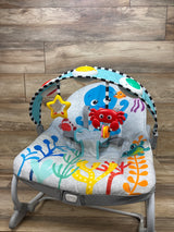 Front view of Baby Einstein Ocean Explorers Opus rocker showcasing ocean-themed seat and toy bar on a wood floor