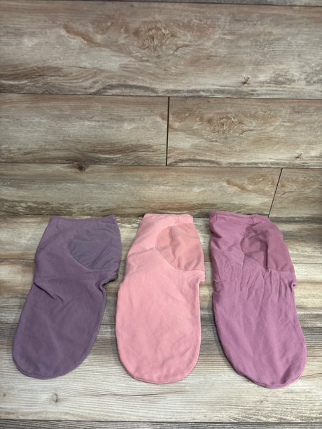 Three Comfy Cubs swaddle wraps in shades of purple and pink on a wooden surface.