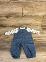 Top-down view of baby 2-piece: white striped long-sleeve shirt and blue overalls with bear bib and leg snaps on wood