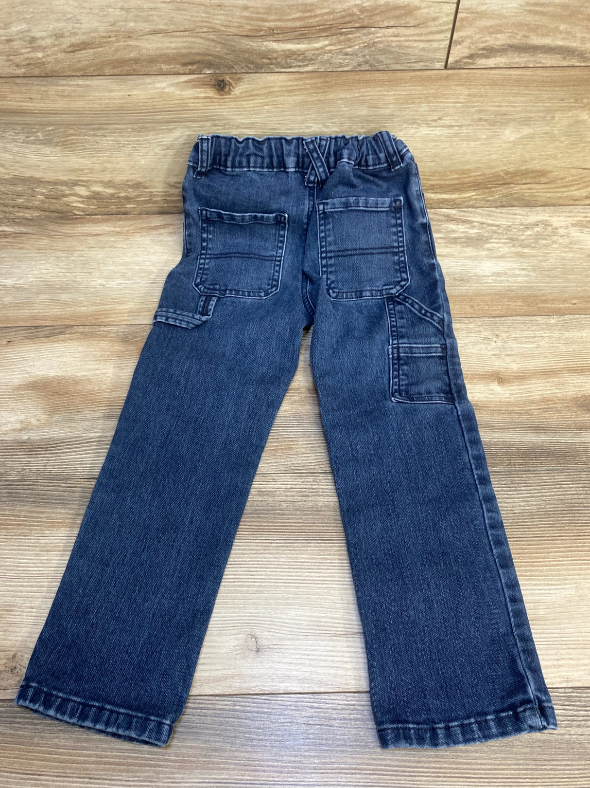 Dark denim kids jeans with elastic waistband and back pockets on wood floor