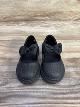Front view of black glitter Mary Jane flats with grosgrain bow straps and lug sole on wood background