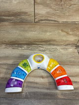 Top-down view of Baby Einstein Glow & Discover Light Bar showing rainbow light-up animal buttons and center spinning rattle on wood floor