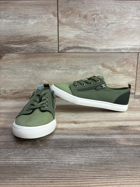 Green canvas kids sneakers with white rubber soles and side zipper detail on wooden surface