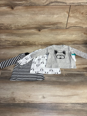 Flat lay of 3-pack baby long-sleeve shirts (3M) showing a grey top with a large dog face, a white dog-print top, and a black-and-white striped top on a wooden floor