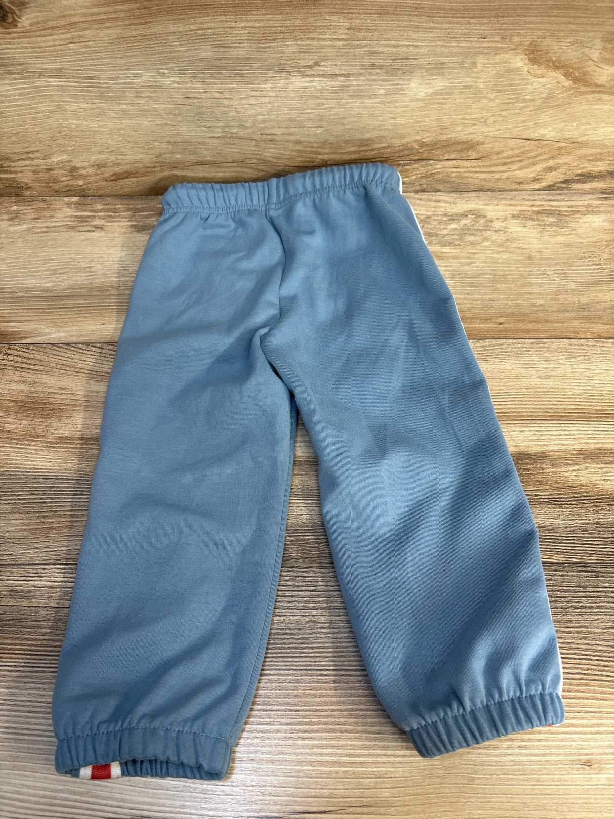 Light blue kids joggers with elastic waist and cuffs, laid flat on wood floor