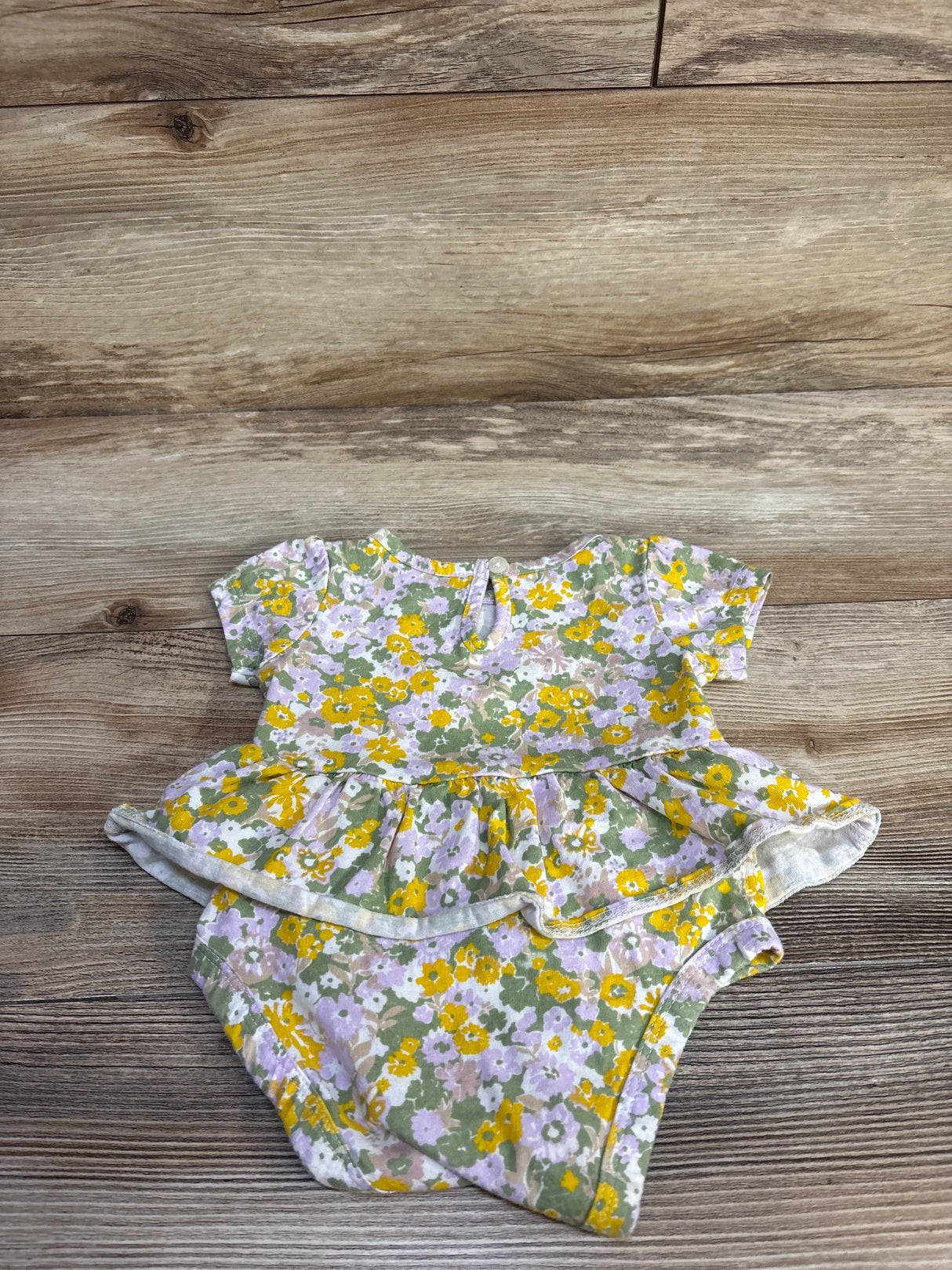Flat lay of Carter's green floral skirted bodysuit showing short sleeves, peplum skirt, and snap closures on wood background