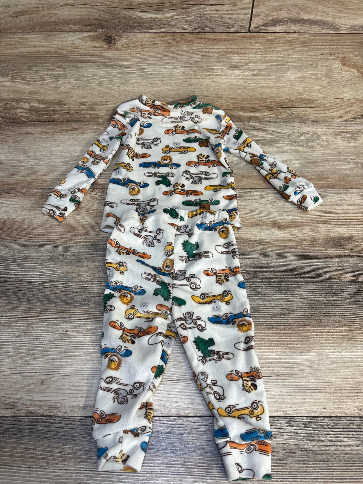 Long sleeve baby pajama set with colorful animal and car print on wood floor