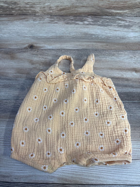 Flat lay of orange gauze baby romper 3 to 6 months with embroidered white daisies, ruffle straps and snap closures on wood