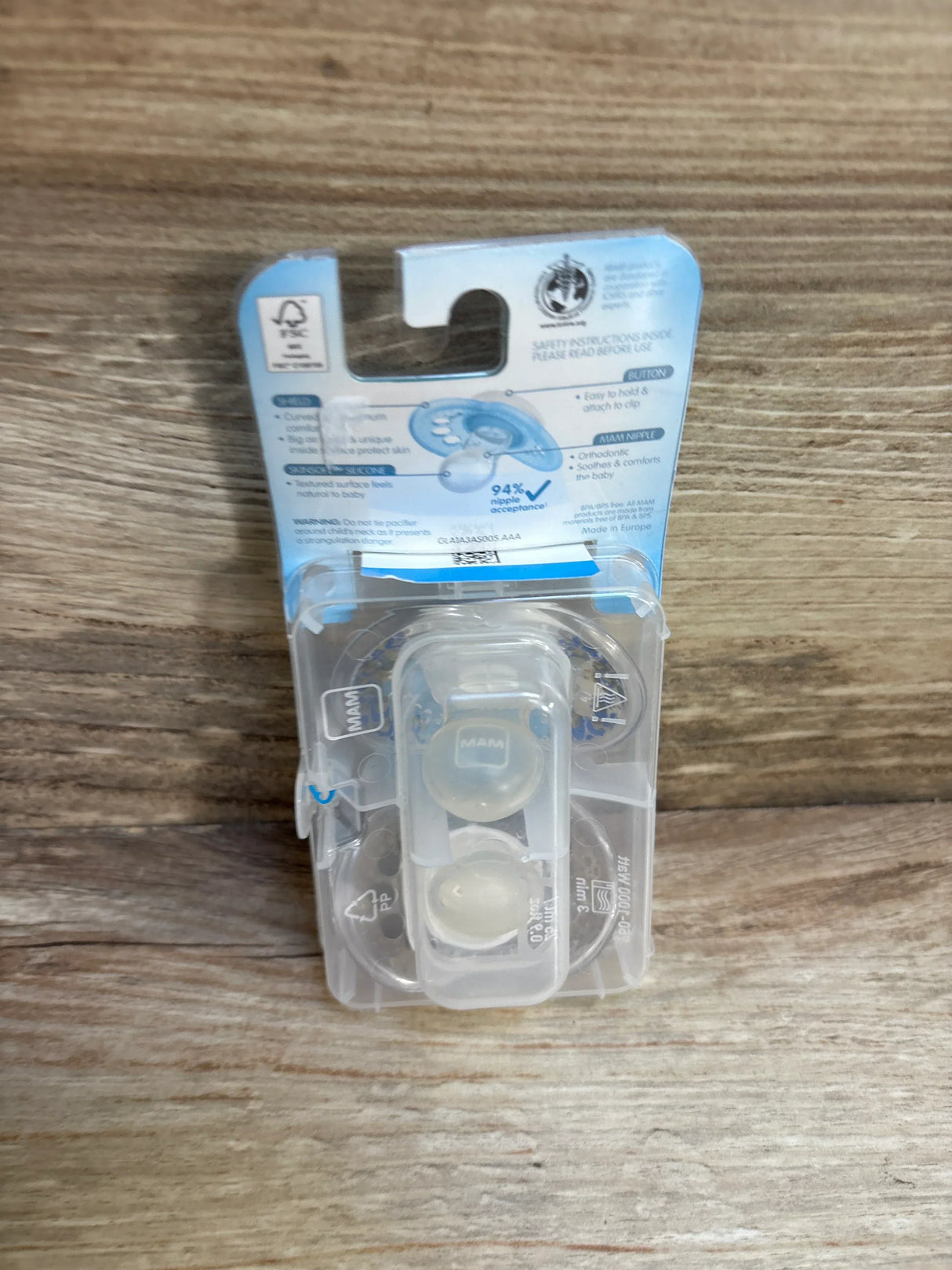 Packaged silicone baby pacifiers in clear case on wood background
