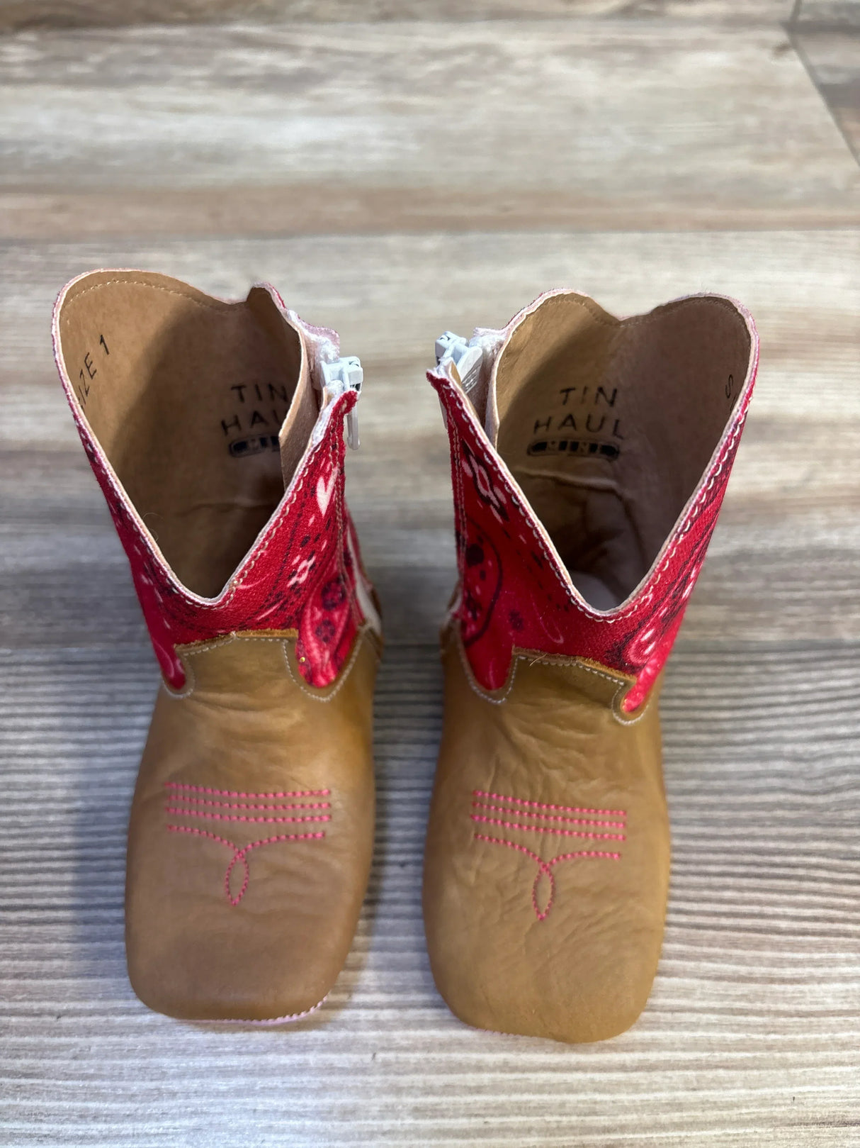 Toddler brown cowboy boots with red bandana print tops on wood floor