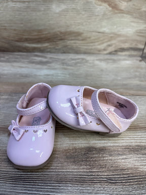 Three-quarter view of Teeny Toes pink patent Mary Jane flats showcasing heart-shaped cutouts, bows, and Velcro strap on a light wood background