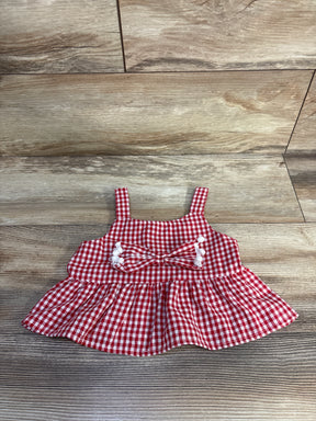 Top-down view of red gingham peplum baby shirt with front bow and white pom-pom trim on wood floor