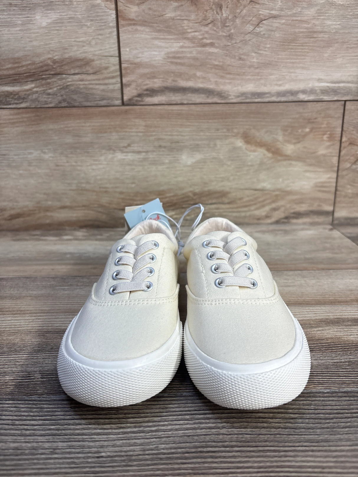 Front view of Cat & Jack Tyler toddler slip-on sneakers in off-white, size 13C, showing textured white rubber soles and elastic laces on wood background