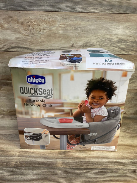 Front view of Chicco QuickSeat portable hook-on chair box showing gray seat with tray and smiling toddler on wooden tabletop