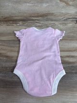 Flat lay of pink Rivalry Threads baby bodysuit showcasing ruffled short sleeves and white leg trim on light wood background