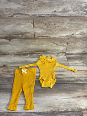 Flat lay of newborn Rachel Zoe yellow ribbed long-sleeve bodysuit and matching bottoms with ruffled collar, snap crotch, and white bow on wood background