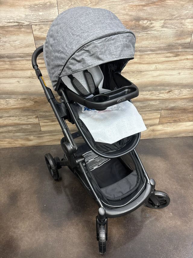 Gray Graco baby stroller with canopy and tray on a wood and concrete floor background