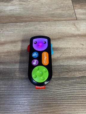Top-down view of Fisher Price Laugh and Learn remote showcasing lit purple face, ABC and 1 2 3 buttons and green d-pad on wood floor