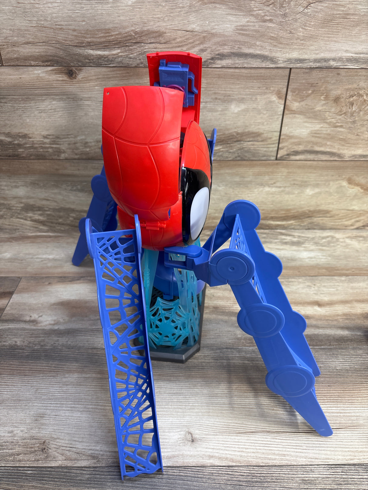 Angled view of Spidey Web-Quarters playset showing red Spider-Man cockpit and blue folding web ramps on wood backdrop