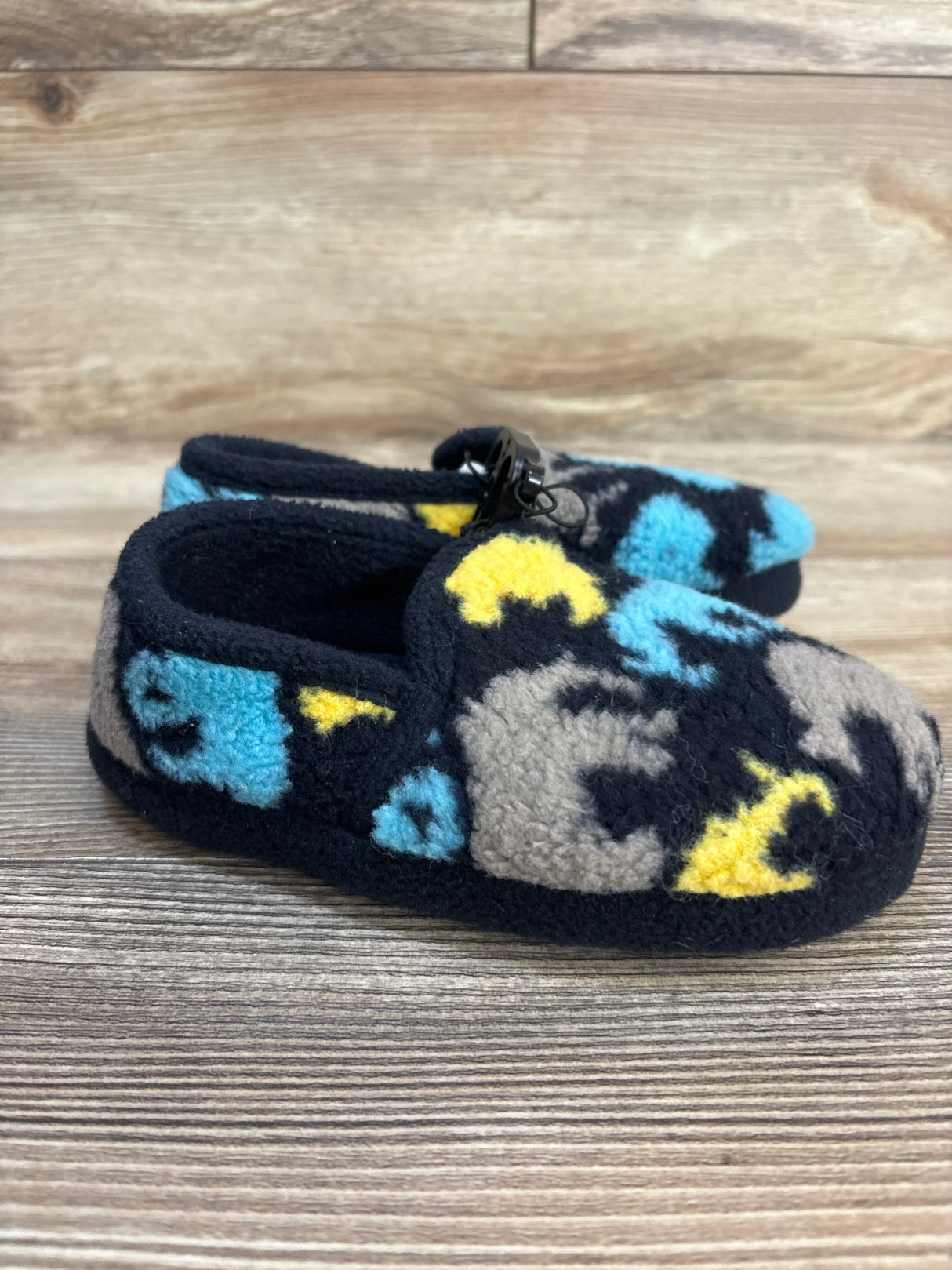 Fleece baby slippers with blue, yellow, and gray camo pattern on wood background