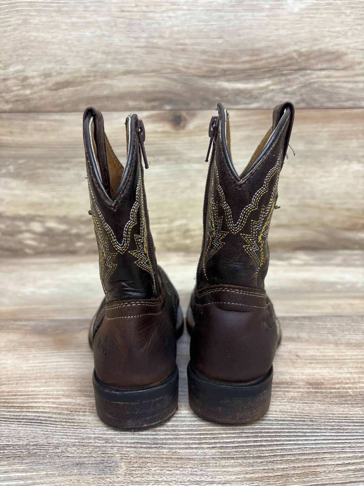 Rear view of Texas Gold Minors brown square toe kids cowboy boots showcasing black and gold stitched shafts on a wood background