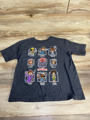 Flat lay of grey kids Stranger Things t-shirt with nine cartoon characters and central Code Red demogorgon on wood background