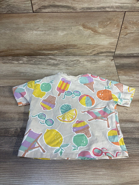 Flat-lay of H&M short-sleeve baby shirt (cream, 9m) showing colorful summer prints, including lemons, ice cream cones, and sunglasses, on wood background
