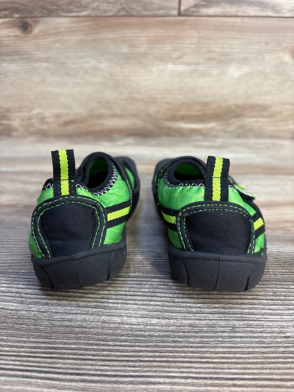Green and black toddler shoes with yellow stripes on wooden floor, rear view