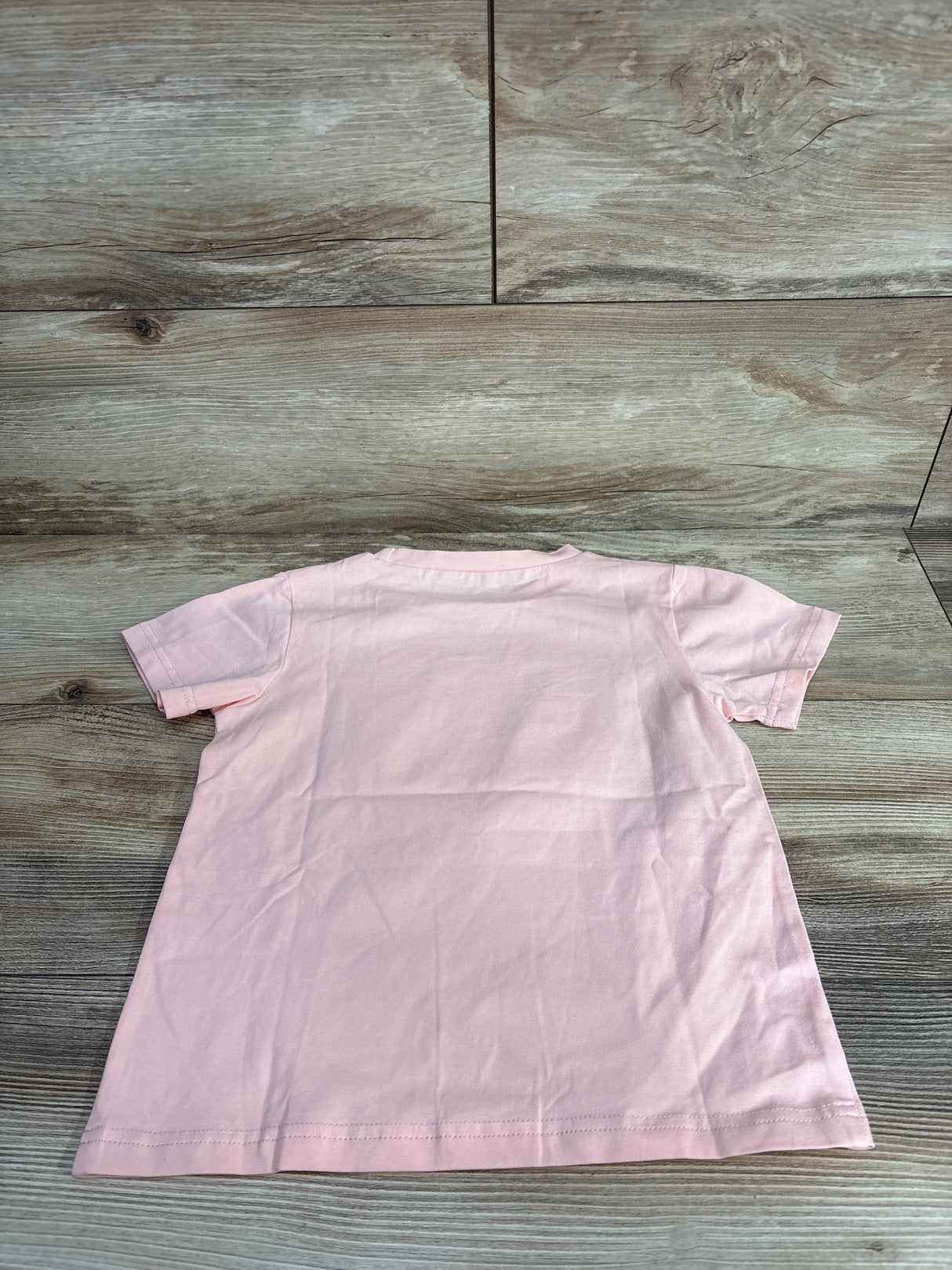 Back view of plain light pink short-sleeve toddler t-shirt on wooden floor