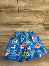 Flat lay of blue Baby Shark swim trunks showing elastic waistband and colorful shark characters on tropical-leaf print on wood floor