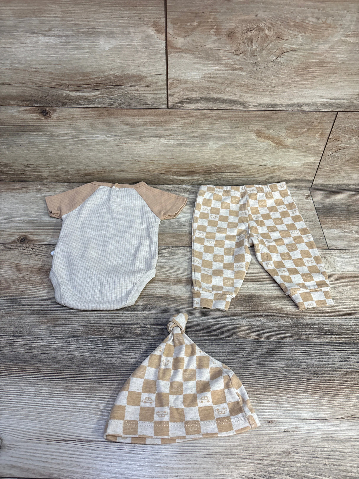 Flat lay of beige Tahari Baby 3-piece ribbed bodysuit, checkered pants, and knotted hat on wood background