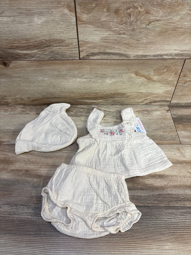 Top-down of beige 3-piece baby set size 3M, embroidered floral top, ruffled bloomers, and matching knot hat on wood background