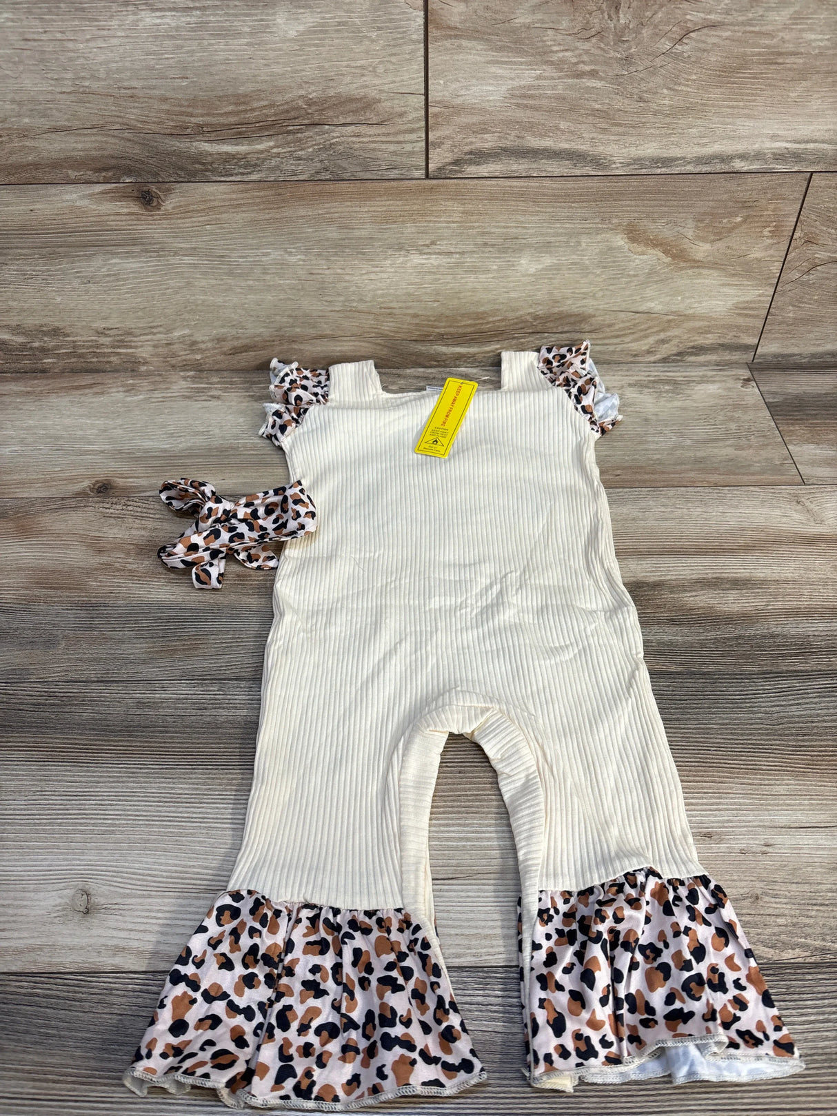Toddler cream ribbed romper with leopard ruffle sleeves, matching headband on wood floor