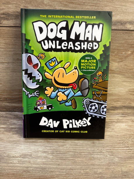 Front view of Dog Man Unleashed hardcover showing green cover with cartoon dog and visible title on a wood background