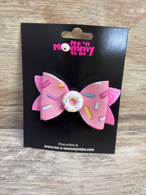 Front view of pink glitter hair bow with sprinkle print and white donut button on a black display card over wood surface
