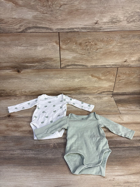 Flat lay of H&M organic 2-pack newborn bodysuits showing white apple-print and solid sage green on wood background