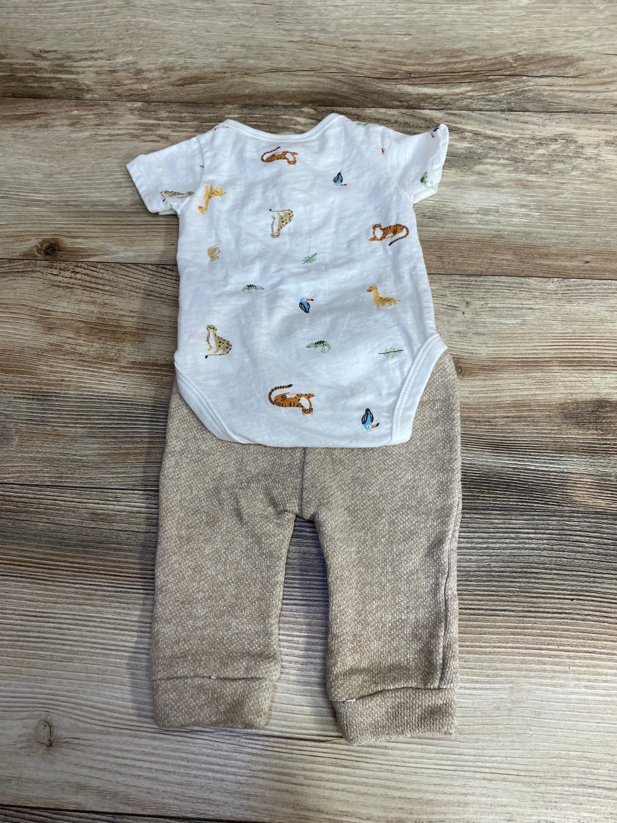 Baby outfit with white animal print bodysuit and beige pants on wood background